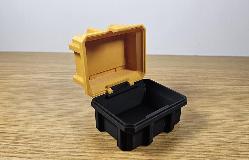 May include: A small, yellow plastic storage box with a black lid. The lid is open and the box is empty.
