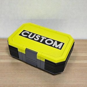 May include: A rectangular storage box with a bright yellow lid and a gray base. The lid features the word "CUSTOM" in bold white letters. The box has a multi-layered design with black accents.