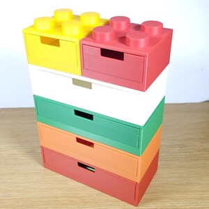 May include: A stack of five colorful drawer units, each with a different color: yellow, red, white, green, orange, and red. The top two units have a Lego-like design with raised studs.