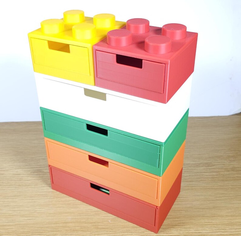 May include: A stack of five colorful drawer units, each with a different color: yellow, red, white, green, orange, and red. The top two units have a Lego-like design with raised studs.
