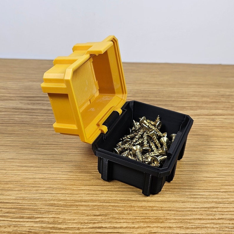 May include: A small yellow plastic storage box with a black lid is open and filled with gold-colored screws.