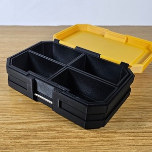 May include: A black plastic storage box with multiple compartments. The box has a yellow lid that is open. The box is sitting on a wooden surface.