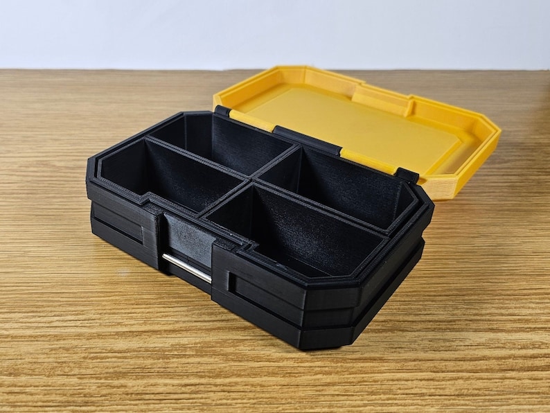 May include: A black plastic storage box with multiple compartments. The box has a yellow lid that is open. The box is sitting on a wooden surface.