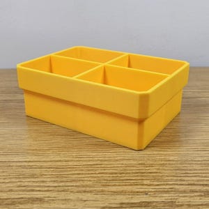 May include: A bright yellow, rectangular organizer with six compartments. The organizer is made of a solid material and has a clean, modern design. The compartments are evenly sized and ready to hold small items.