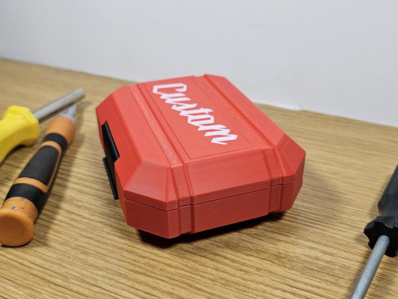 May include: A red plastic case with the word "CUSTOM" printed in white on the top. The case is closed and has a black latch on the side.