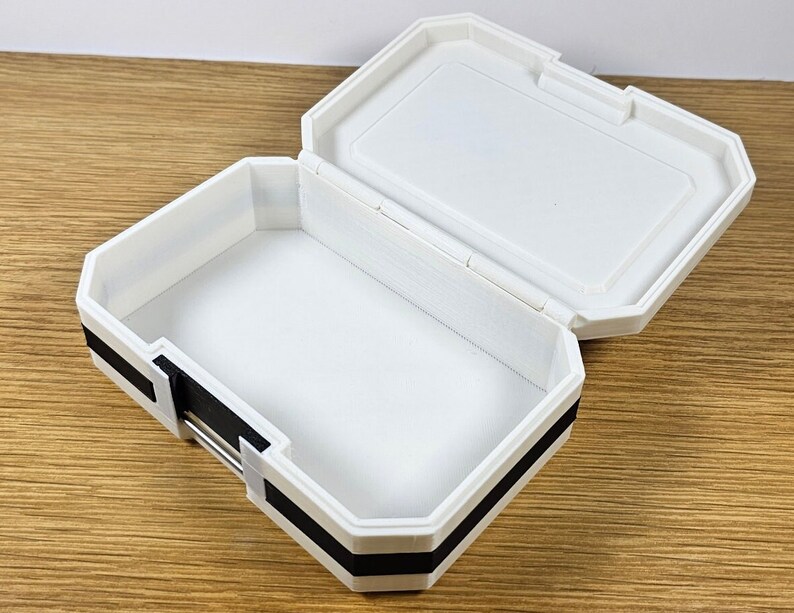 Puede incluir: Caja de pl&aacute;stico blanca con ribete negro. La caja est&aacute; abierta y el interior est&aacute; vac&iacute;o.