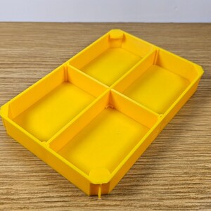 May include: A yellow plastic tray with four compartments. The tray is empty.