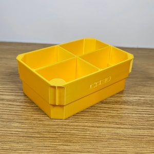 May include: A yellow plastic storage box with four compartments. The box has the word "CREO" printed on the bottom.