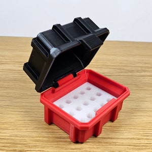 May include: A red and black hinged storage box with a white foam insert. The box is open, revealing the interior with multiple circular cutouts. The lid is black and has a textured design.