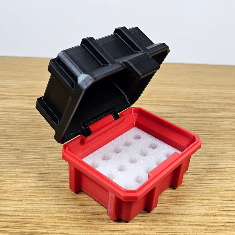 May include: A red and black hinged storage box with a white foam insert. The box is open, revealing the interior with multiple circular cutouts. The lid is black and has a textured design.