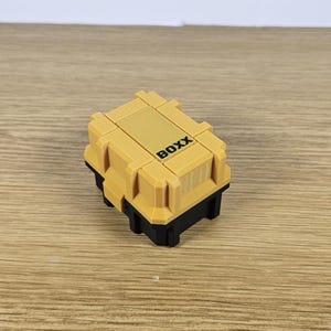 May include: A small, yellow plastic box with the word "BOXX" printed on the top. The box has a black base.