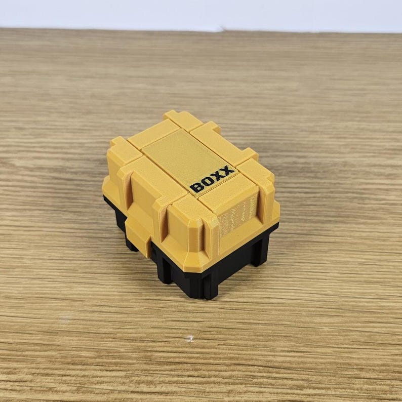 May include: A small, yellow plastic box with the word "BOXX" printed on the top. The box has a black base.