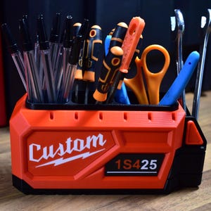 May include: An orange and black tool organizer with the word "Custom" in white script. The organizer holds pens, screwdrivers, scissors, and wrenches. The text "1S425" is also visible on the organizer.