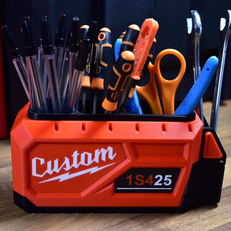 May include: An orange and black tool organizer with the word "Custom" in white script. The organizer holds pens, screwdrivers, scissors, and wrenches. The text "1S425" is also visible on the organizer.