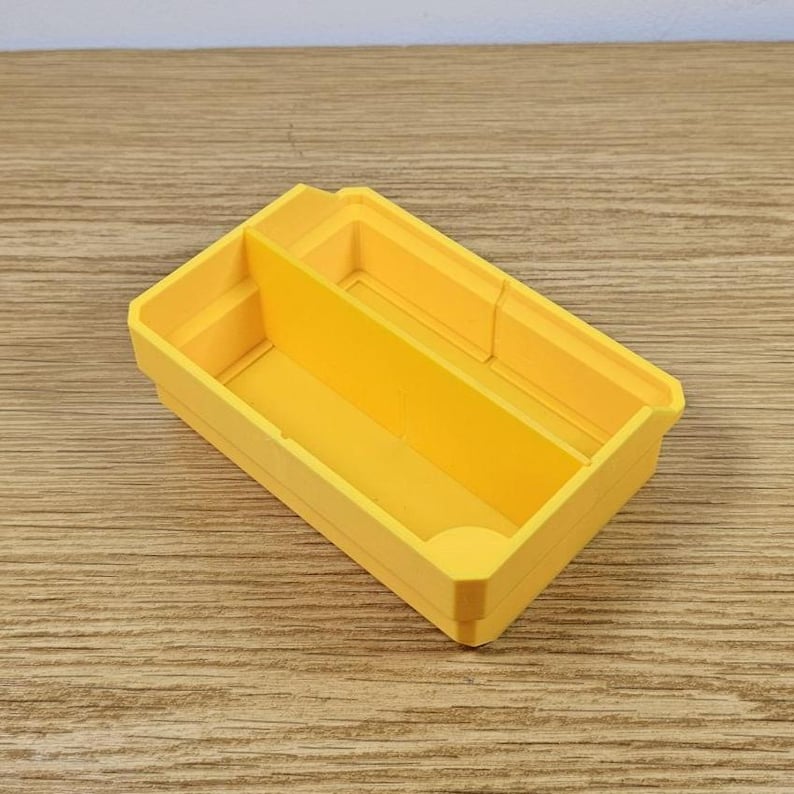 May include: A bright yellow rectangular organizer with two compartments. The organizer is made of plastic and sits on a wooden surface. The compartments are divided by a vertical divider, creating two separate storage spaces.