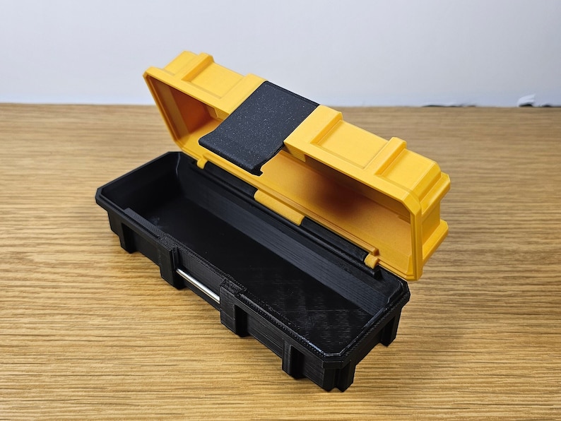 K&ouml;nnte beinhalten: Eine kleine, gelbe und schwarze Plastik-Werkzeugbox mit einem Scharnierdeckel. Der Deckel ist ge&ouml;ffnet und zeigt das leere Innere der Werkzeugbox.