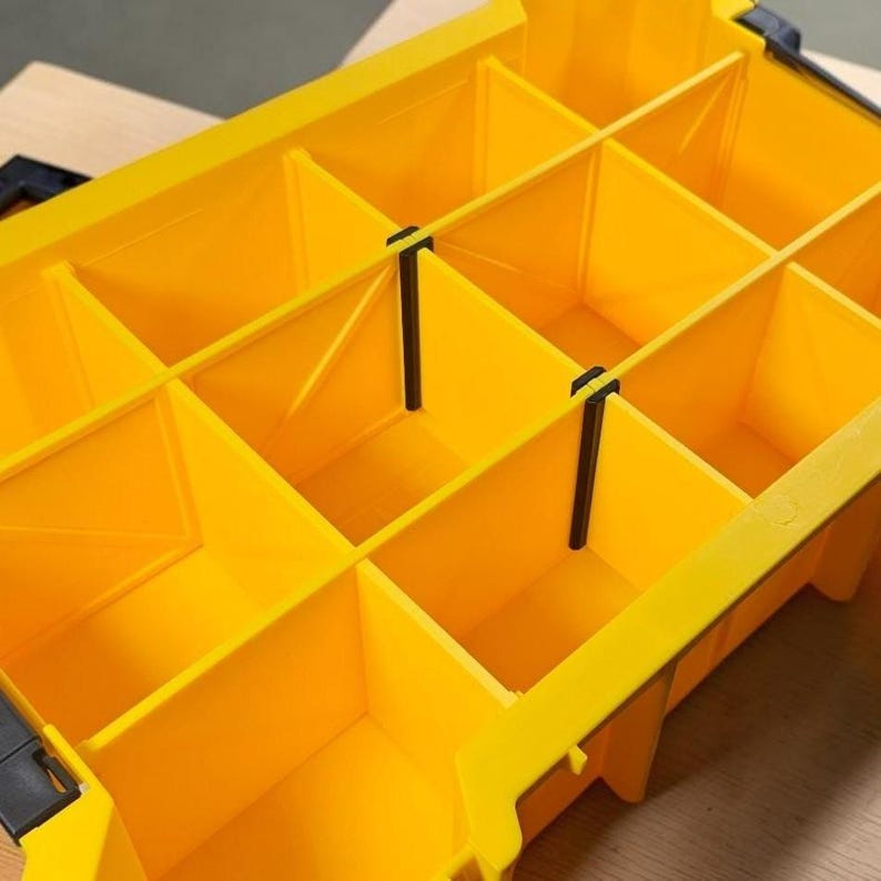 May include: A bright yellow plastic storage organizer box featuring multiple rectangular compartments separated by removable dividers. The container includes black plastic locking latches on the sides and a grid-like interior structure for sorting small items.