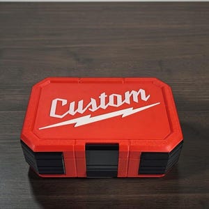 May include: A red and black tool case with the word "Custom" in white script and a white lightning bolt design. The case is rectangular with a textured surface and a hinged lid. The case is likely used for storing tools.