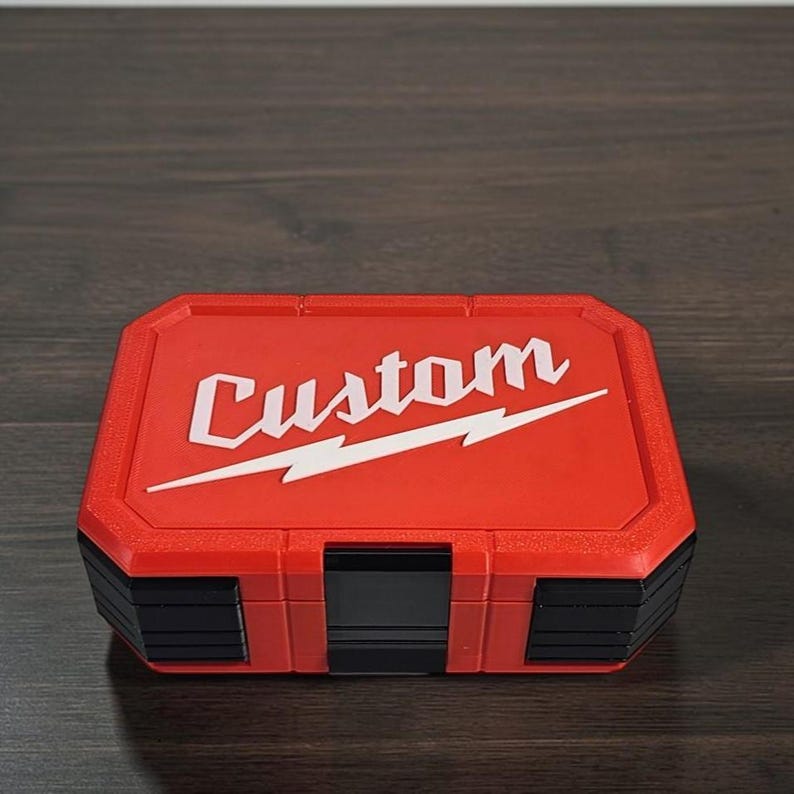 May include: A red and black tool case with the word "Custom" in white script and a white lightning bolt design. The case is rectangular with a textured surface and a hinged lid. The case is likely used for storing tools.