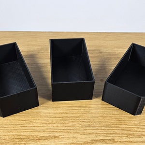 May include: Three black rectangular boxes made of plastic. The boxes are empty and have a smooth surface.