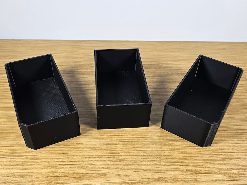 May include: Three black rectangular boxes made of plastic. The boxes are empty and have a smooth surface.
