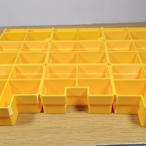 May include: A yellow plastic parts organizer with multiple compartments. The organizer is rectangular and has a grid-like structure, with each compartment being a small, open-top box. The compartments are arranged in rows and columns.