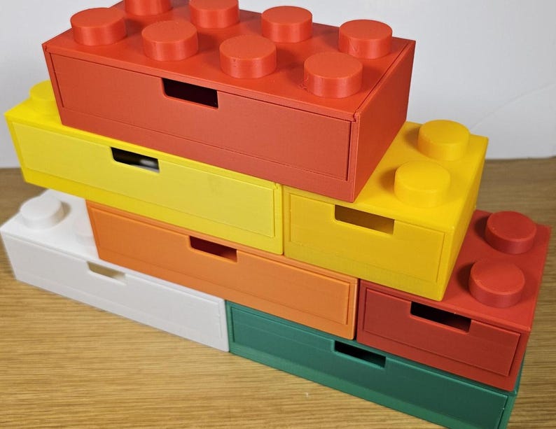 May include: A set of six colorful drawer organizers shaped like Lego bricks. The drawers are stacked on top of each other, with the top drawer being red, the second yellow, the third orange, the fourth white, the fifth green, and the bottom drawer red.
