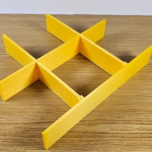 Op de afbeelding: Een gele plastic organizer met vier vakken. De organizer is kruisvormig en heeft een vierkante opening in het midden.