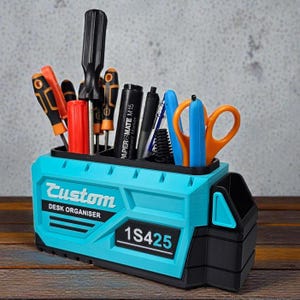 May include: A custom desk organizer in turquoise and black, holding various tools and stationery. The organizer features the word "Custom" and "DESK ORGANISER" printed on the front, along with the number "1S425". Screwdrivers, pens, and scissors are visible.