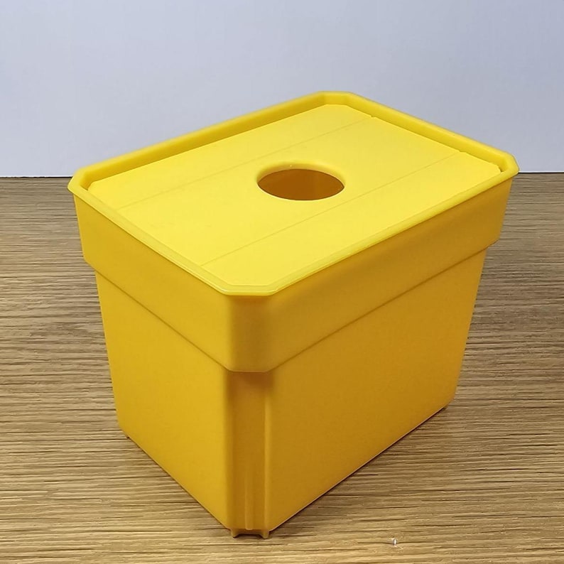 Pode incluir: Um recipiente de pl&aacute;stico amarelo com uma tampa e um furo no topo. O recipiente &eacute; projetado para conter e dispensar itens como len&ccedil;os de papel ou guardanapos.