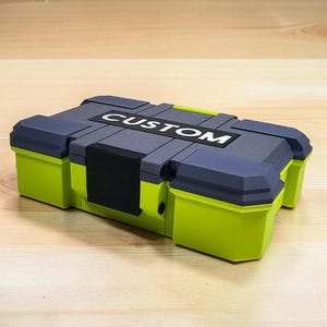Peut inclure: Un conteneur de stockage rectangulaire avec le mot "CUSTOM" en lettres blanches. Le conteneur est principalement vert citron avec des accents gris et noirs. Le couvercle est gris avec une poign&eacute;e noire.