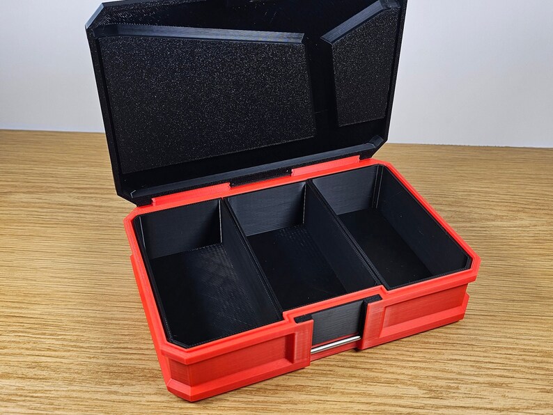 May include: Red plastic storage box with three compartments. The box is open and the compartments are empty.