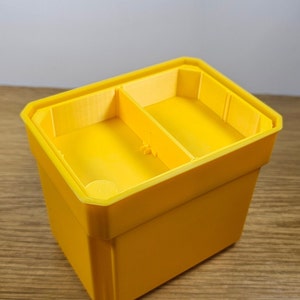 May include: A yellow plastic divided storage box with two compartments. The box is empty and has a smooth, glossy finish.