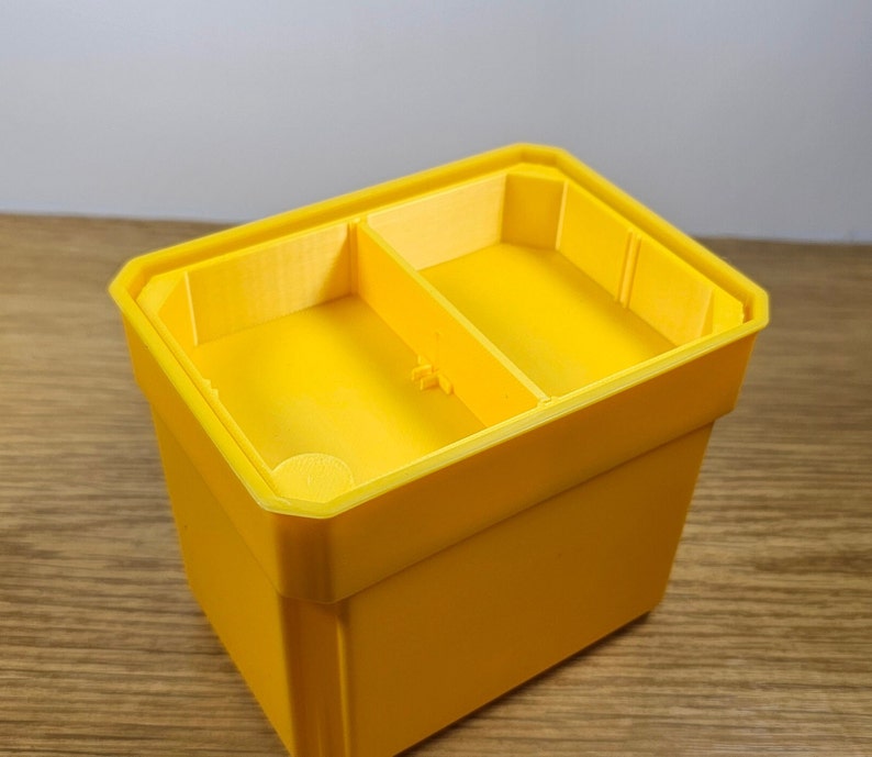 May include: A yellow plastic divided storage box with two compartments. The box is empty and has a smooth, glossy finish.