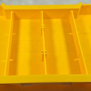 May include: Bright yellow plastic storage container with four internal dividers. The container has black handles on each end with the text "TOUGH SYSTEM". The container is designed for organising and storing tools or other items.
