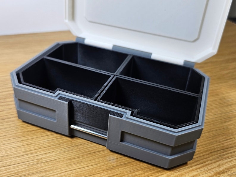 K&ouml;nnte beinhalten: Eine graue Plastik-Aufbewahrungsbox mit einem Scharnierdeckel und mehreren F&auml;chern. Die Box ist ge&ouml;ffnet und die F&auml;cher sind leer.