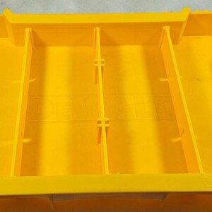 May include: Bright yellow storage container with internal dividers. Black handles on each end with the text "TOUGH SYSTEM". The container is designed for organizing and transporting tools and equipment.
