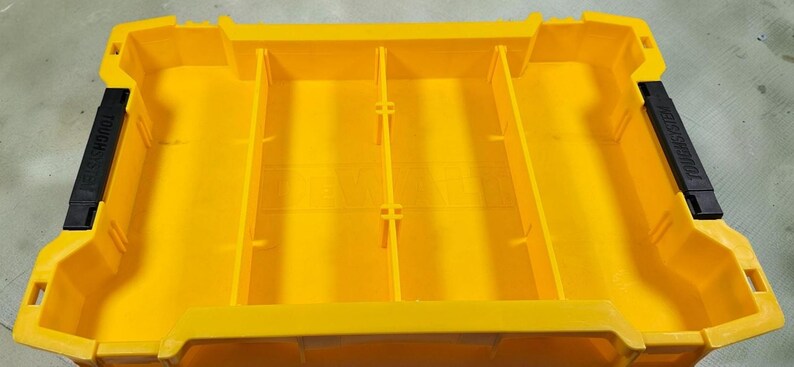 May include: Bright yellow storage container with internal dividers. Black handles on each end with the text "TOUGH SYSTEM". The container is designed for organizing and transporting tools and equipment.