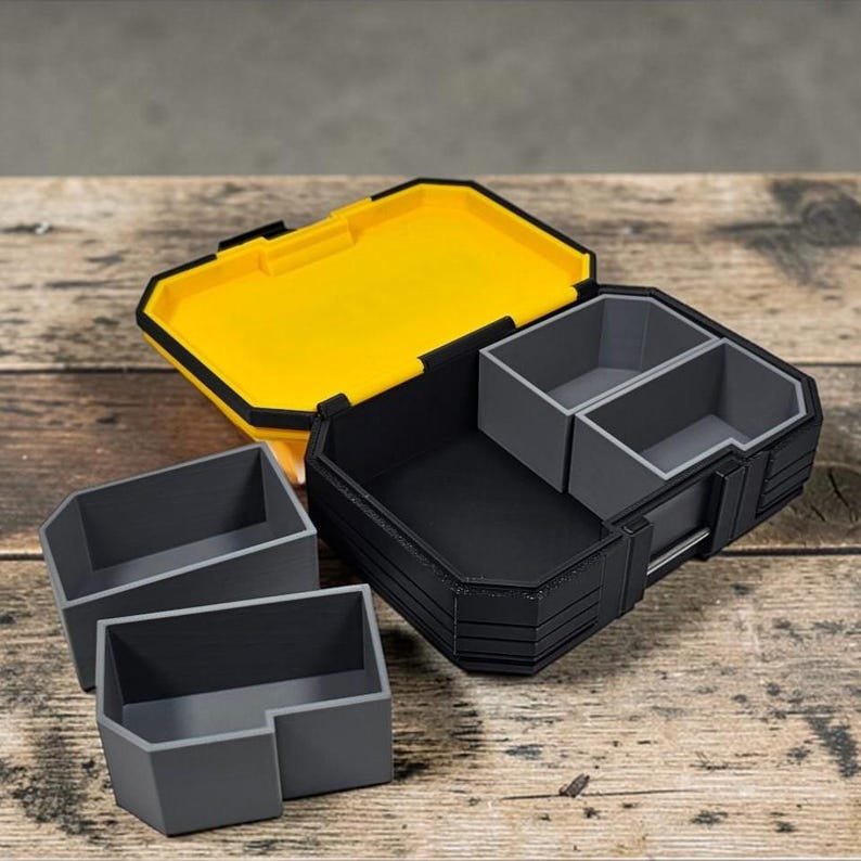 May include: A black and yellow storage box with a hinged lid and two gray interior compartments. Two additional gray storage containers are in front of the box. The box is open, revealing the interior. The box is on a wooden surface.