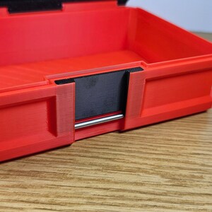 May include: Red plastic storage box with a black latch and a silver metal handle. The box is open and the inside is visible.