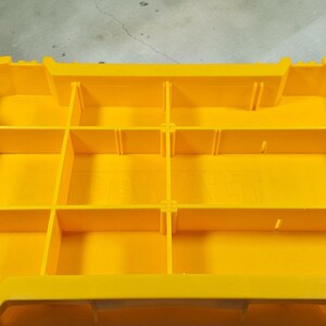 May include: Bright yellow plastic organizer with multiple compartments. Features black handles on each side. The organizer is designed for storing and organizing small items.