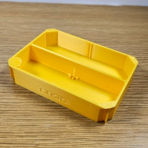 May include: A yellow plastic tray with two compartments. The tray has a raised edge and a smooth surface.