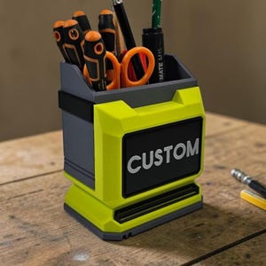 May include: A two-tone desk organiser in bright yellow and grey. The organiser features the word "CUSTOM" in white on a black rectangle. It holds various tools, including screwdrivers and scissors.