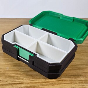 May include: A black and green plastic storage box with four compartments. The lid is open and the compartments are empty.
