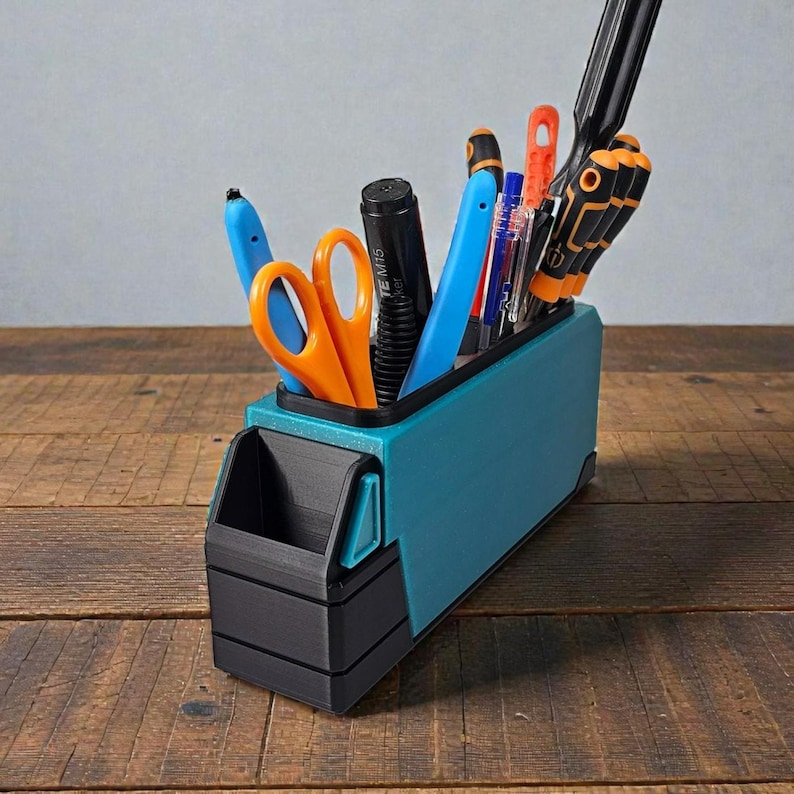 May include: A teal and black desk organizer filled with various office supplies, including pens, scissors, and screwdrivers. The organizer is made of plastic and sits on a wooden surface.