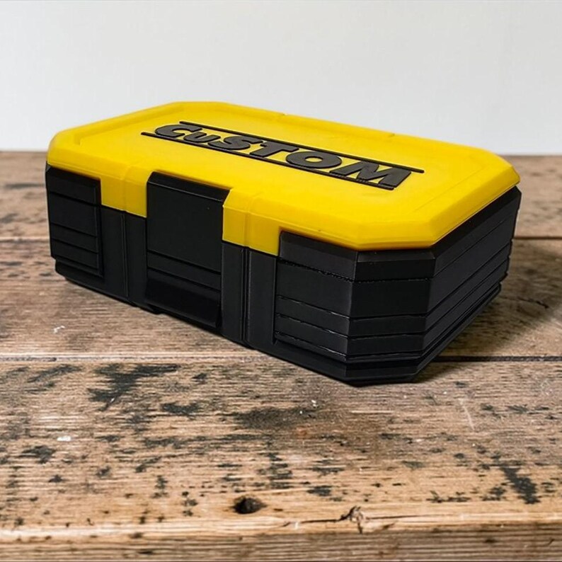 May include: A yellow and black storage box with the word "CUSTOM" in black lettering on the lid. The box has a rectangular shape and is sitting on a wooden surface.