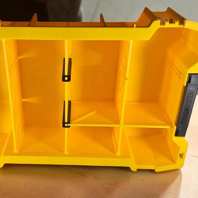 May include: A bright yellow plastic tool organizer tray featuring multiple compartments separated by vertical dividers. The interior base is embossed with the DEWALT logo, and a black handle on the side is labeled with the text TOUGHSYSTEM.