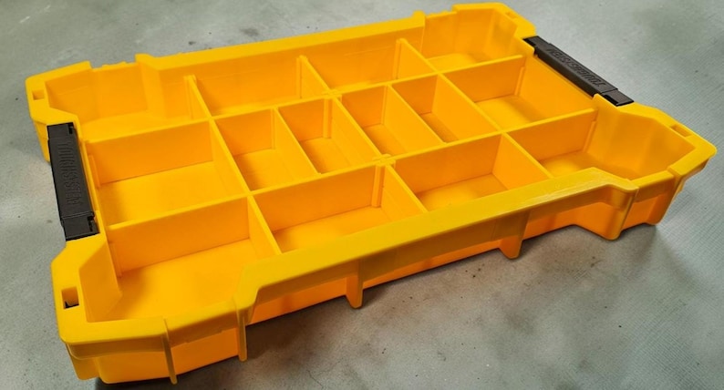 May include: A bright yellow parts organizer with multiple compartments. The organizer has a rectangular shape with a series of dividers creating individual storage spaces. Black handles are on each end.