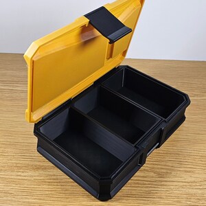 May include: A yellow plastic storage box with a black lid and three compartments. The lid is open and the compartments are empty.