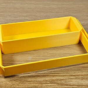 Op de afbeelding: Een gele plastic opbergdoos met deksel. De doos is gemaakt van 3D-geprint plastic en heeft een glad, getextureerd oppervlak.